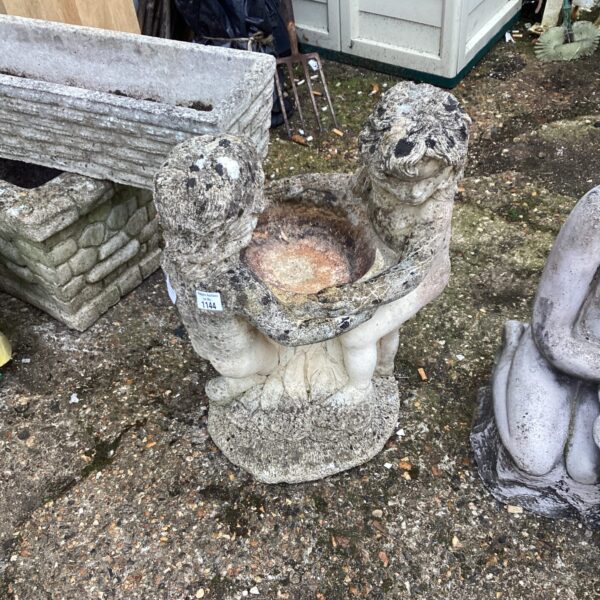 Vintage stone bird bath with two boy figures in a garden setting.