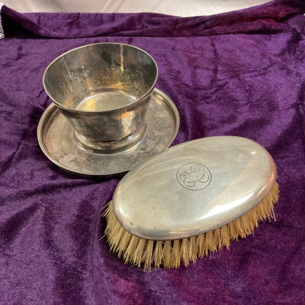 Antique silver hand mirror and silverplate bowl on a table.