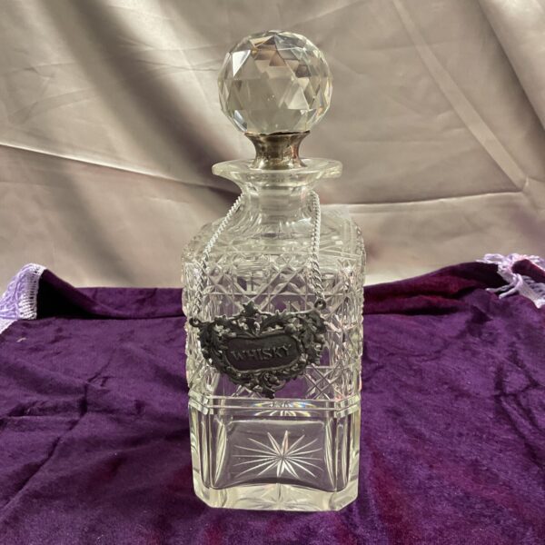 Antique cut glass whiskey decanter with stopper and faceted design.