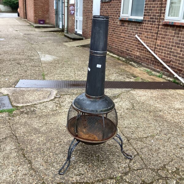 Large metal garden fire pit with spark guard in a garden setting.