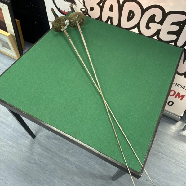Pair of vintage fencing foils displayed on a green surface.