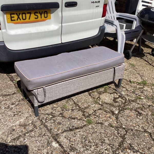 Rafia garden bench with cushion in outdoor setting.