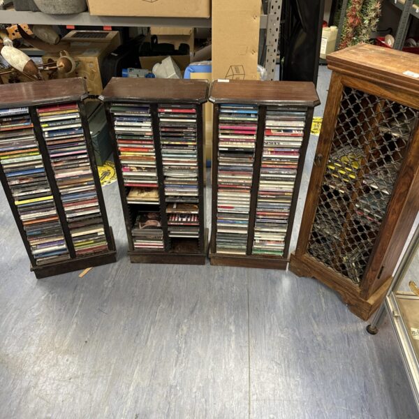 Four wooden CD racks filled with CDs in a home setting.