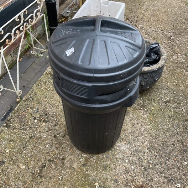 Black plastic rubbish bin in a garden setting.