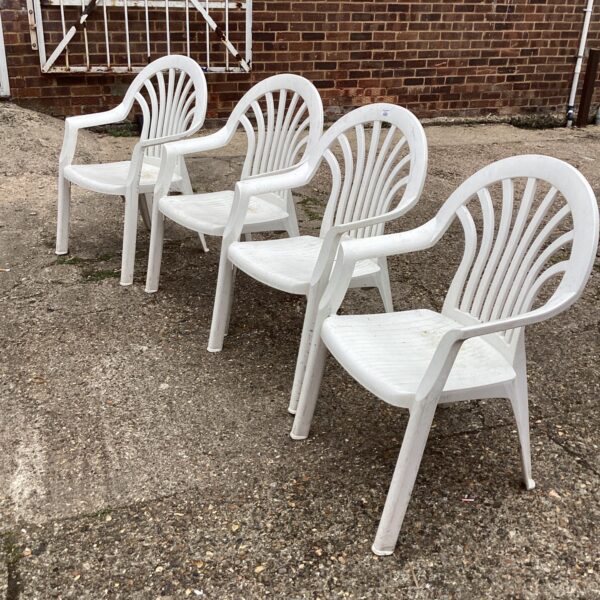 Set of four white plastic garden chairs in a garden setting.
