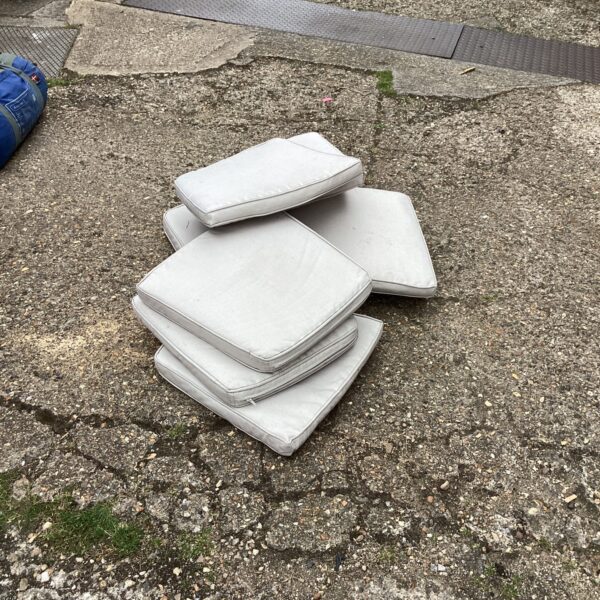 Quantity of neutral-coloured garden chair cushions on a patio.