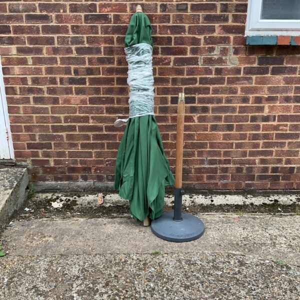 Large green parasol standing in a garden setting.