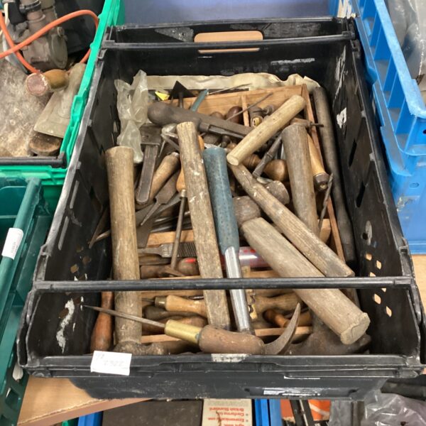 Black crate filled with a variety of metal hand tools, including hammers and chisels.