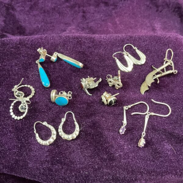 Assorted 925 sterling silver earrings displayed on a dark surface.