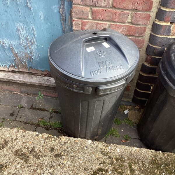 Black plastic garden dustbin for outdoor waste disposal.