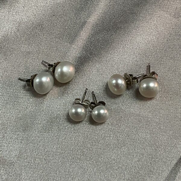 Close-up of three pairs of silver pearl stud earrings.