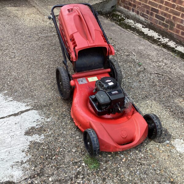 Red Wolf lawn mower for repair in a garden setting.