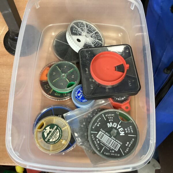 Assorted fishing line weights in a plastic storage box.