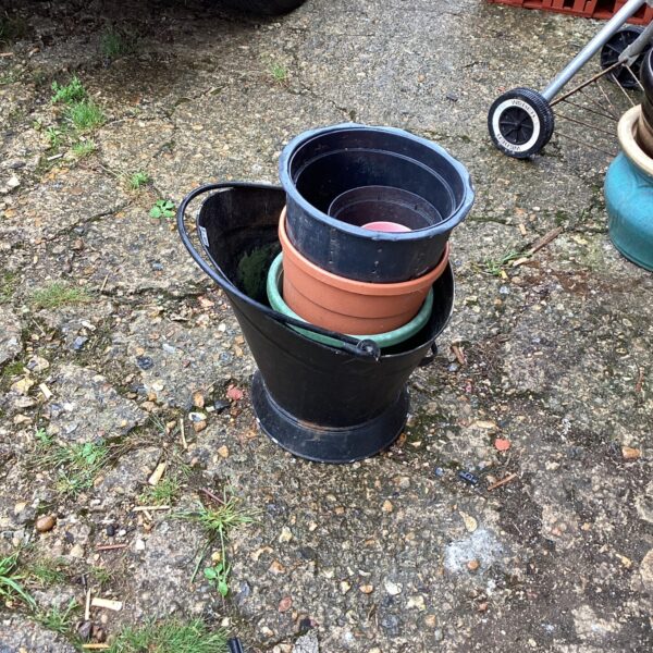 Vintage metal coal bucket with terracotta garden pots in a garden setting.