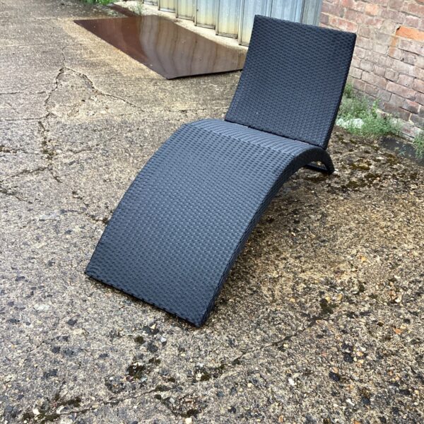Woven rattan sun lounger in a garden setting.