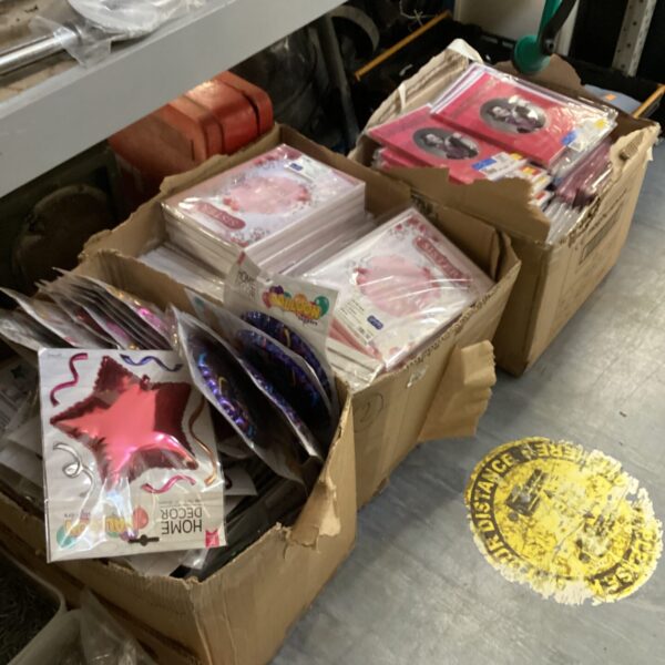 Assorted greeting cards and party supplies in cardboard boxes.