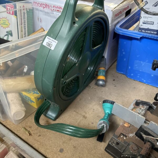 Green garden hose reel with hose attached, showing damage.
