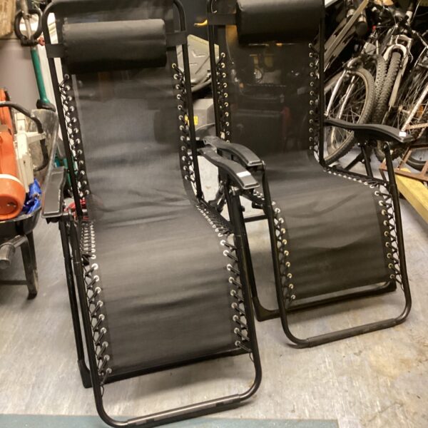 Two black folding garden loungers in a garden setting.