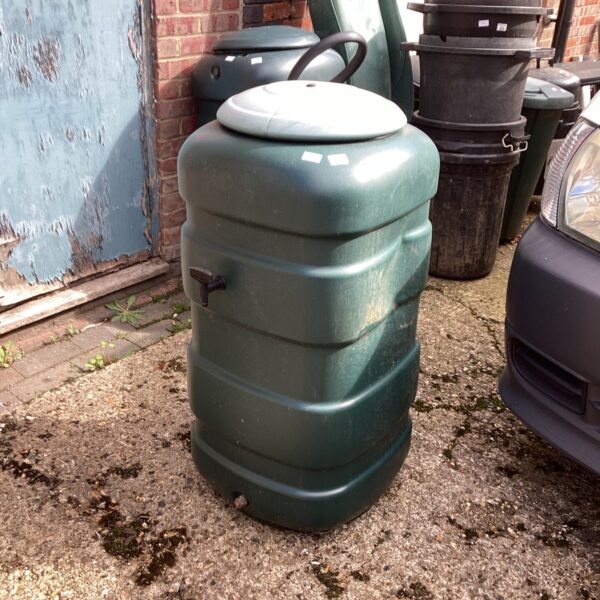 Green plastic water butt in a garden setting for rainwater collection.