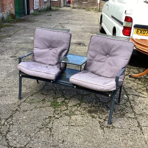 Vintage metal garden seat with patterned cushions in a garden setting.