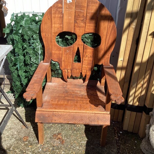 Wooden garden chair with a carved skull backrest for outdoor seating.