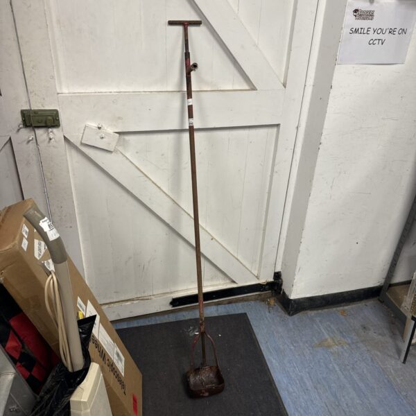Vintage cast iron drain scoop leaning against a wall.