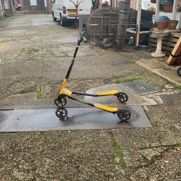 Vintage yellow three-wheeled scooter in a garden setting.