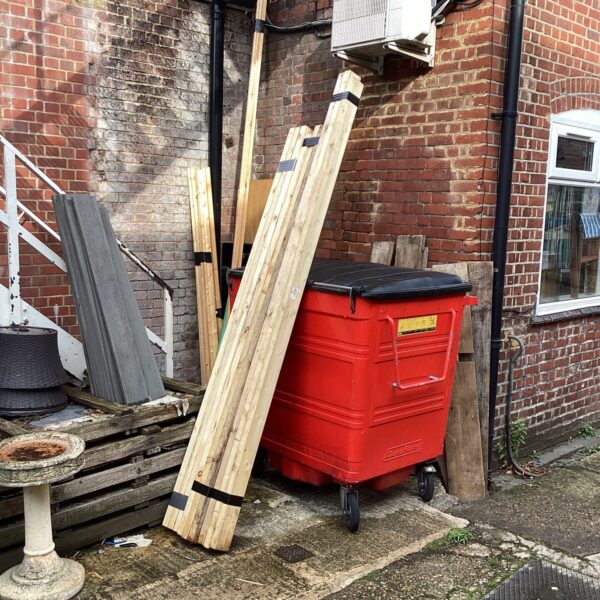 Quantity of planned timber leaning against a red bin.