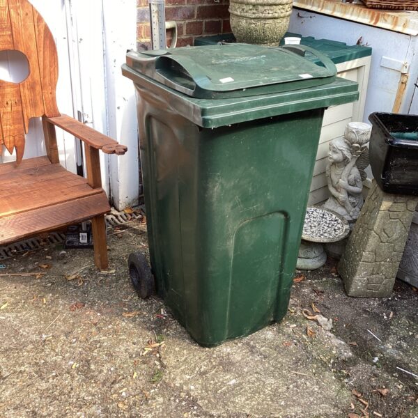 Green garden wheelie bin for outdoor waste storage.