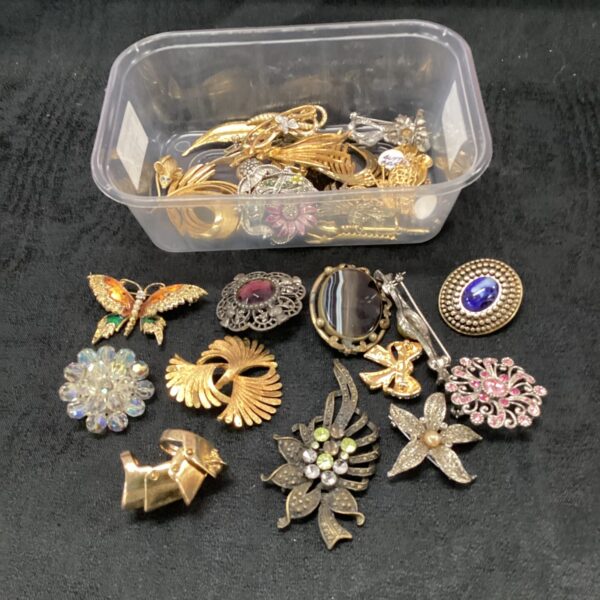 Vintage costume jewellery brooches and pins in a plastic tub.