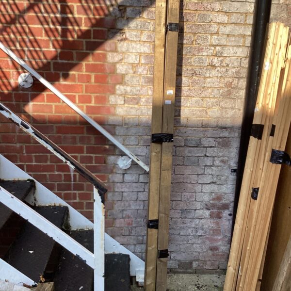 Garden view of timber lengths leaning against a brick wall.