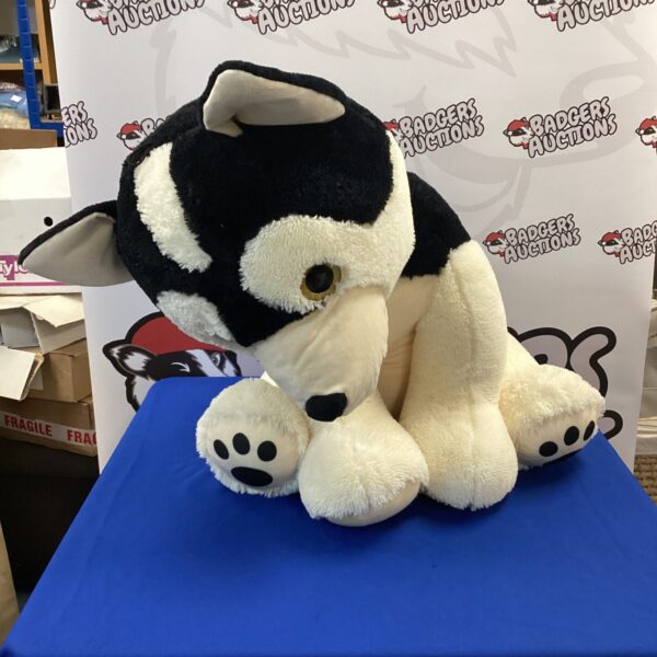Large, black and white dog cuddly toy on blue background.