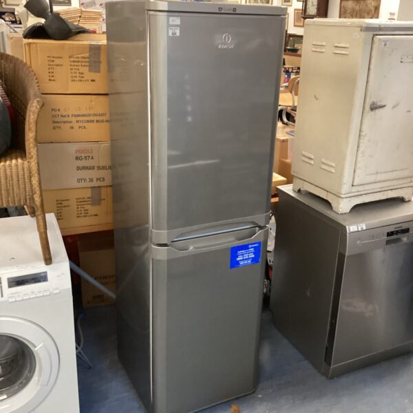 Used Indesit fridge freezer in a cluttered room.