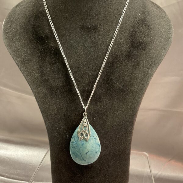 Close-up of a turquoise teardrop necklace with art nouveau pendant.