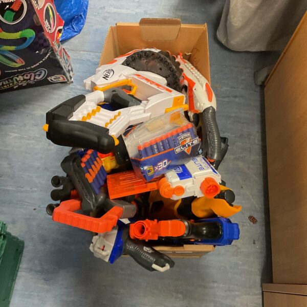 A collection of Nerf blasters and foam darts in a cardboard box.