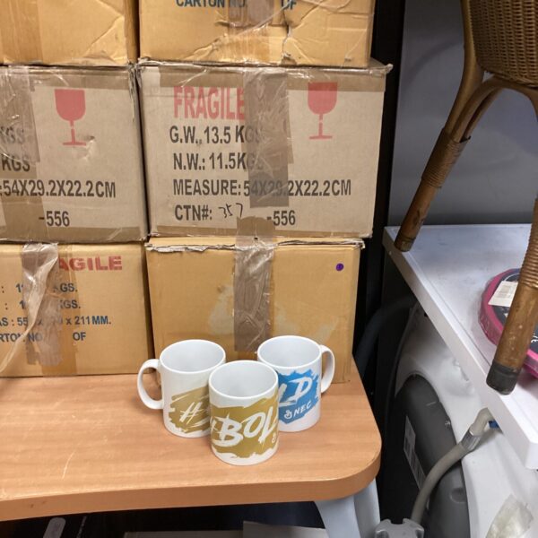 Stacked boxes of Bold & NEC branded promotional mugs.