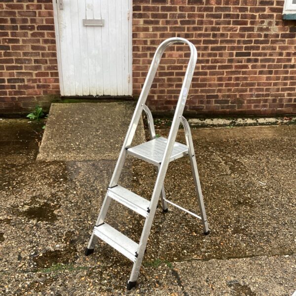 Three-step aluminium ladder against a brick wall.