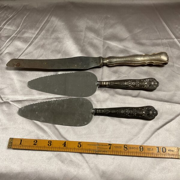 Antique silver pie servers and carving knife set on a cloth background.