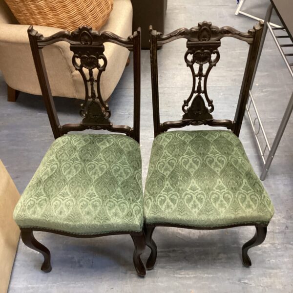 Pair of vintage green upholstered dining chairs with carved wood.