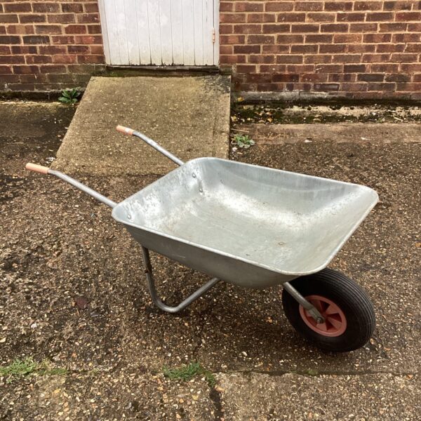 Metal wheelbarrow with a pneumatic tyre in a garden setting.