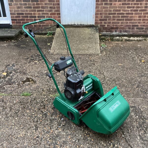 Vintage Qualcast 35s petrol lawnmower in a garden setting.