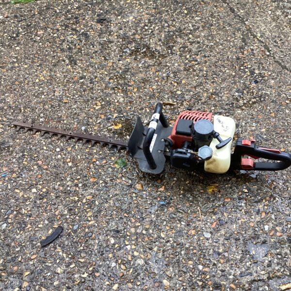 Side view of a used petrol hedge trimmer for garden maintenance.