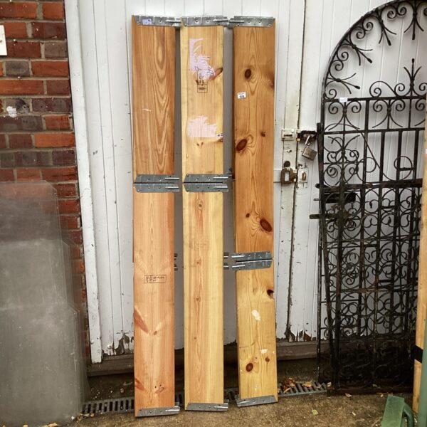 Three sections of folding pine garden borders leaning against a wall.
