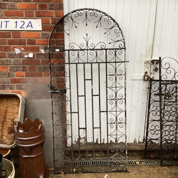 Antique wrought iron gate with Victorian scrollwork in a garden setting.