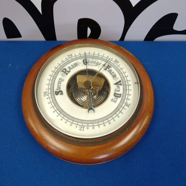Vintage barometer with detailed enamel face and wooden casing.