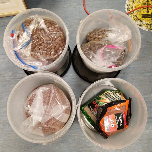 Assorted fishing bait tubs with boilies and pellets for angling.
