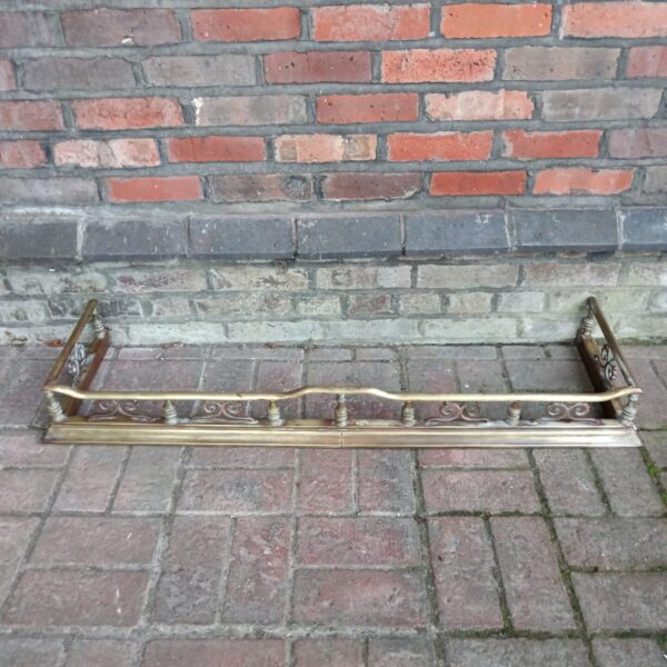 Ornate Victorian brass and copper fireplace fender on a dark surface.
