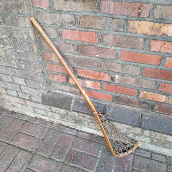 Antique hickory lacrosse stick with woven pocket, vintage sports equipment.
