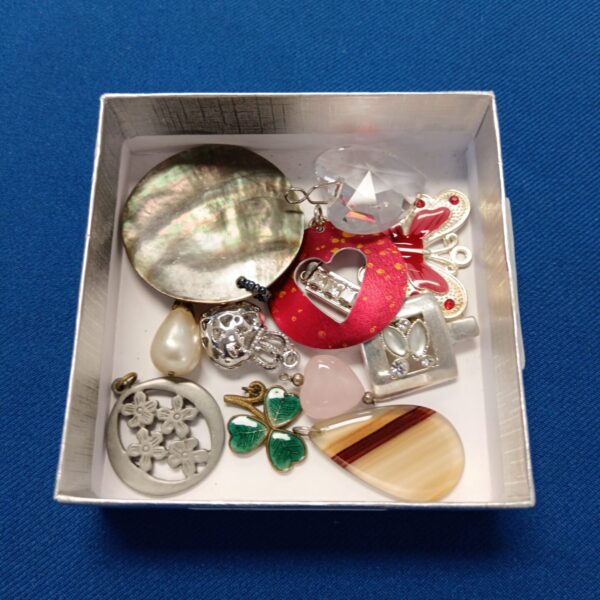 Tray of mixed necklace pendants for crafting or collecting.