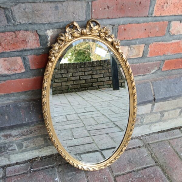 Ornate gilt framed French style oval mirror with bevelled edge.